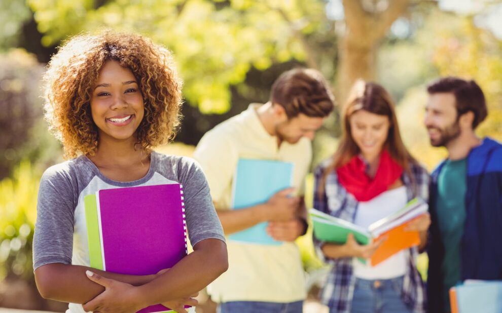 Portrait of college girl holding notes with friends