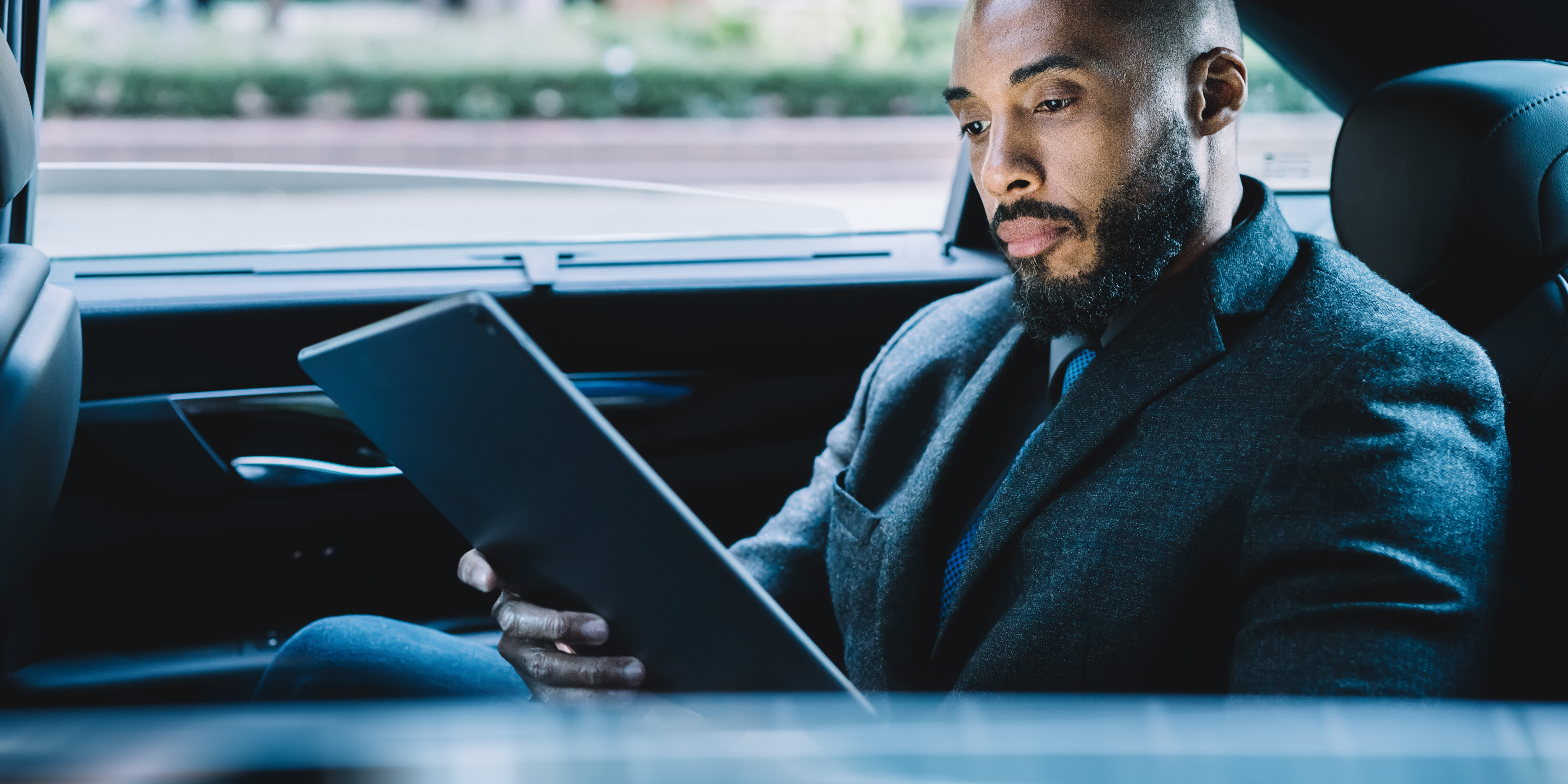 Businessman with black skin sitting on backseat in taxi automobile and searching contact number for making online video conference via modern touch pad, concept of market digitalisation on tablet
