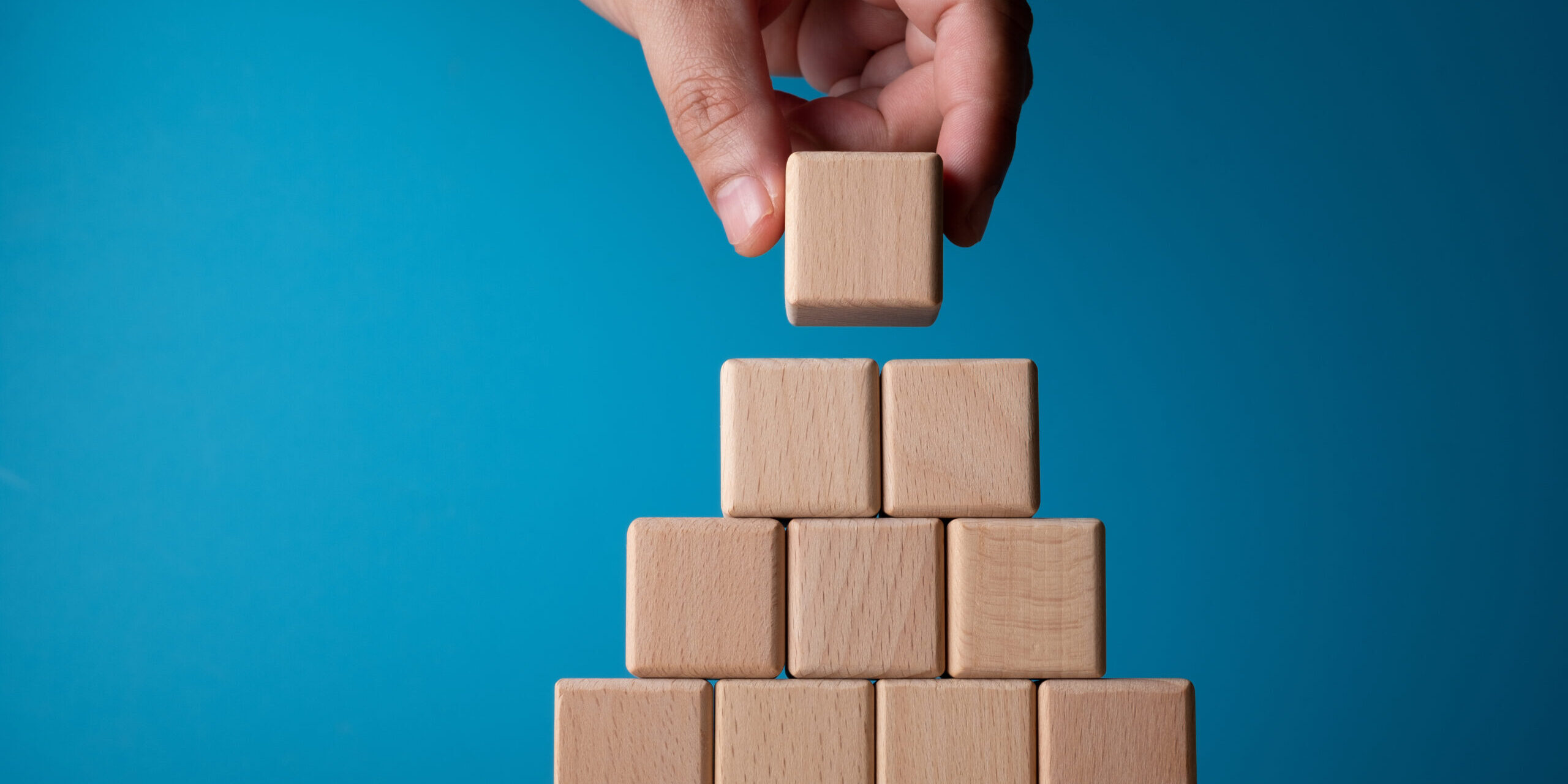 Hand arranging block on blue background. Business concept on progress or building something.