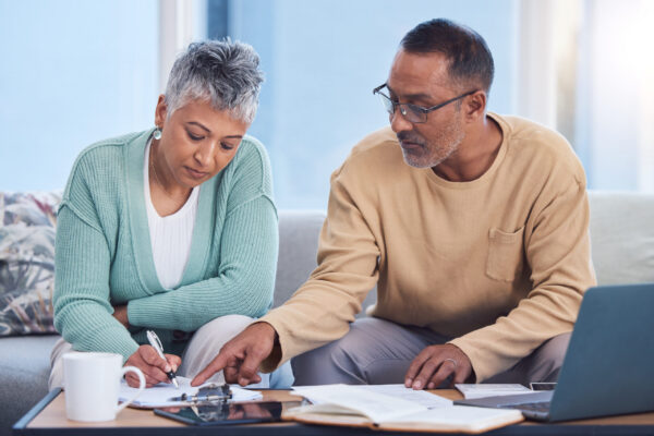 Senior black couple, taxes and home with laptop, documents or focus in home for family finance. Elderly, woman and man with computer, tablet or notebook in audit, budget or planning on lounge sofa taxes in retirement