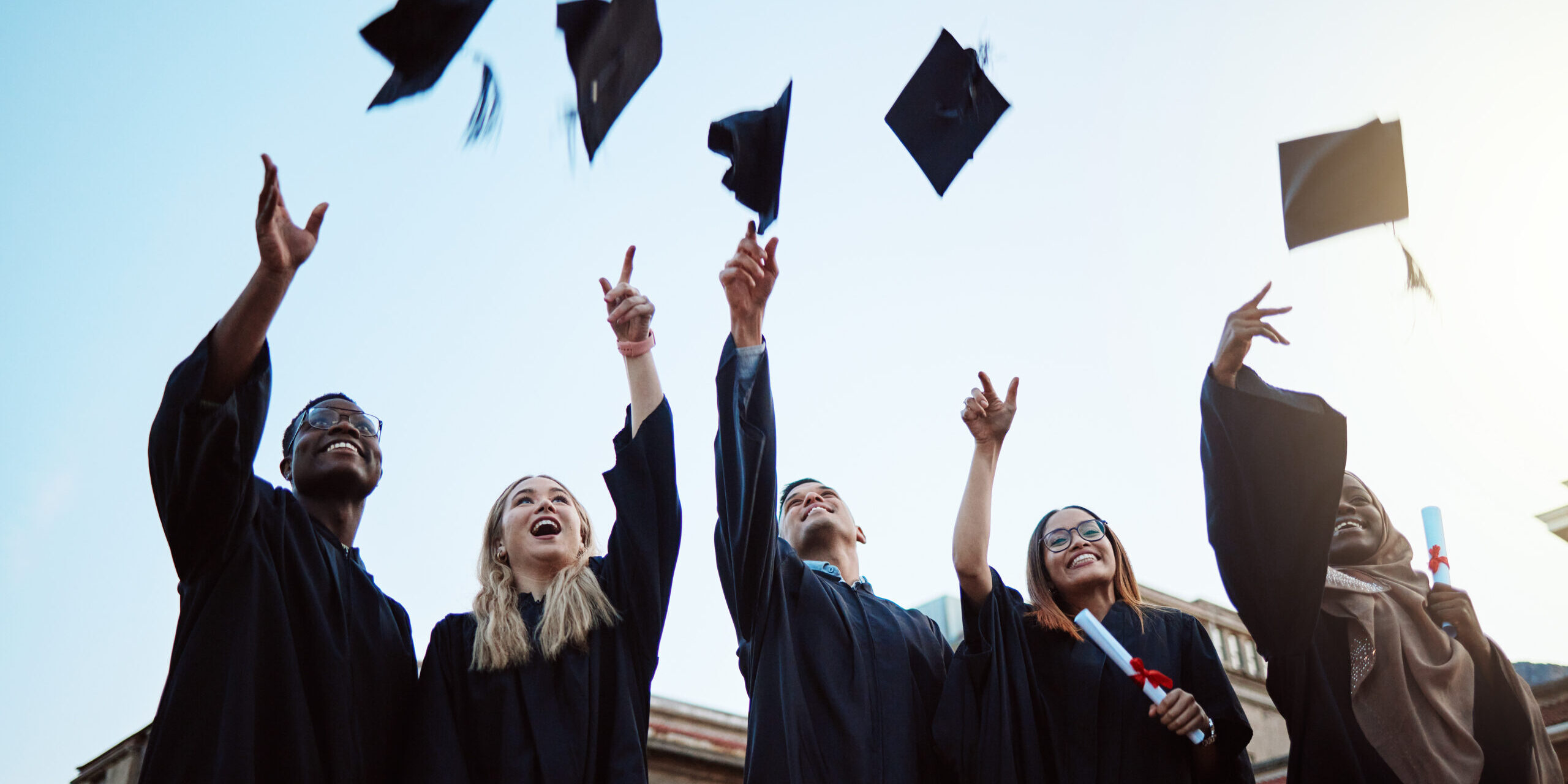 Graduation, education and success with friends in celebration as a graduate group outdoor, throwing mortar caps. Diversity, university and man and woman students celebrating a college diploma Cost of education College