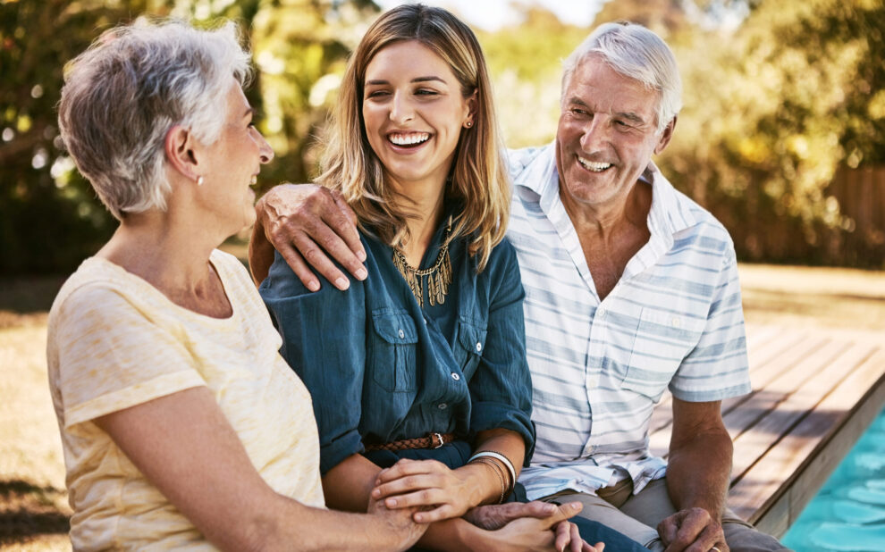 Family, senior parents and woman by pool holding with care, love and hug bonding outdoor. Smile, happy person and people in retirement with adult daughter together with bokeh in nature in summer
