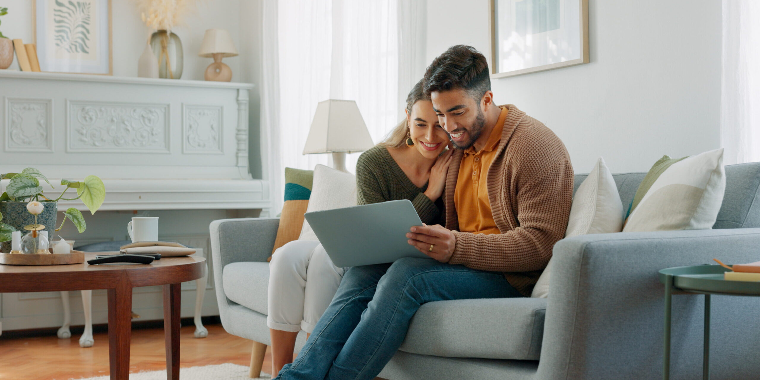 Laptop, living room and couple search website information for home investment, loan or real estate property discussion on sofa. Young people on couch with pc internet, planning future together
