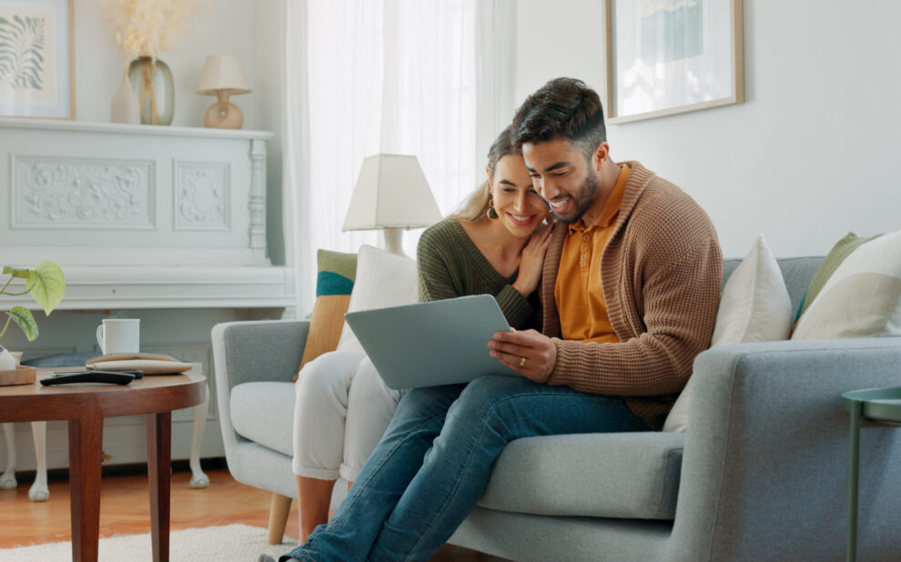 Laptop, living room and couple search website information for home investment, loan or real estate property discussion on sofa. Young people on couch with pc internet, planning future together
