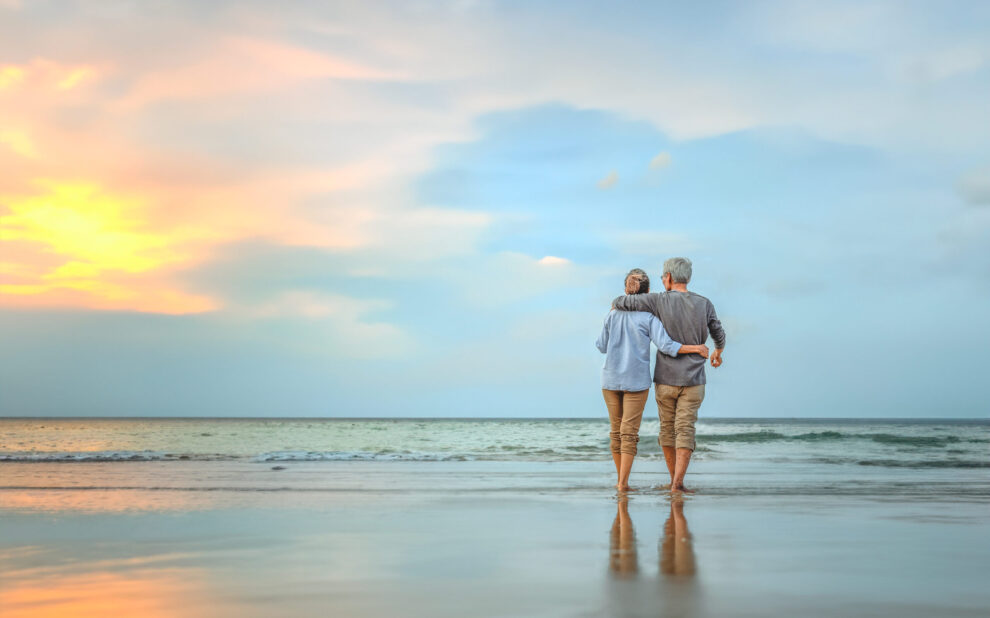 Senior couple walking on the beach holding hands at beach sunrise in evening. Life Insurance in Retirement