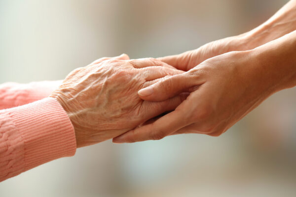 Old and young holding hands on light background, closeup